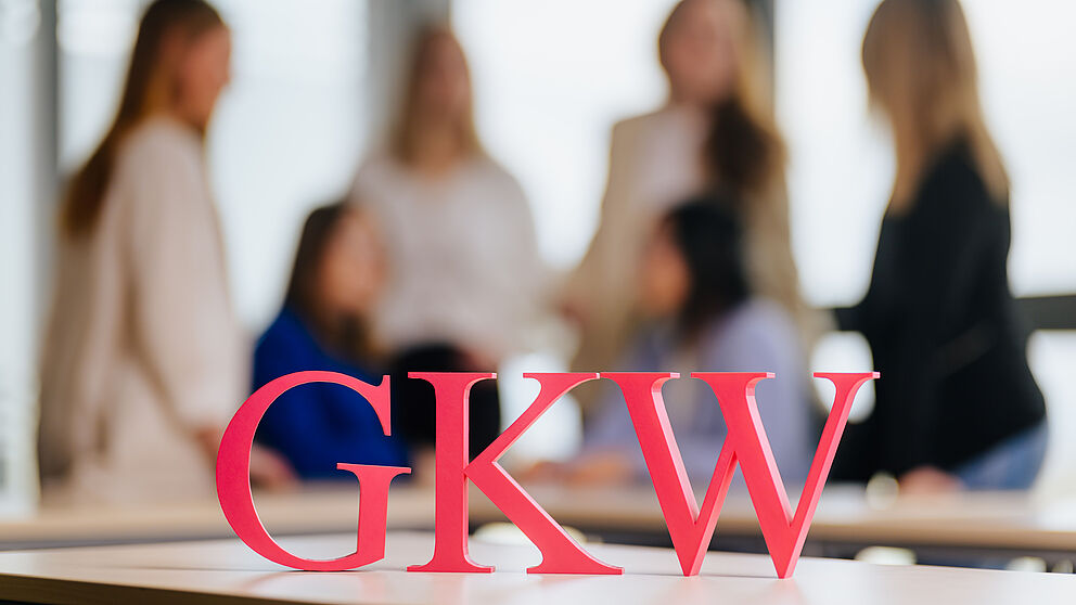 Menschen unscharf im Hintergrund, im Vordergrund die Buchstaben GKW.