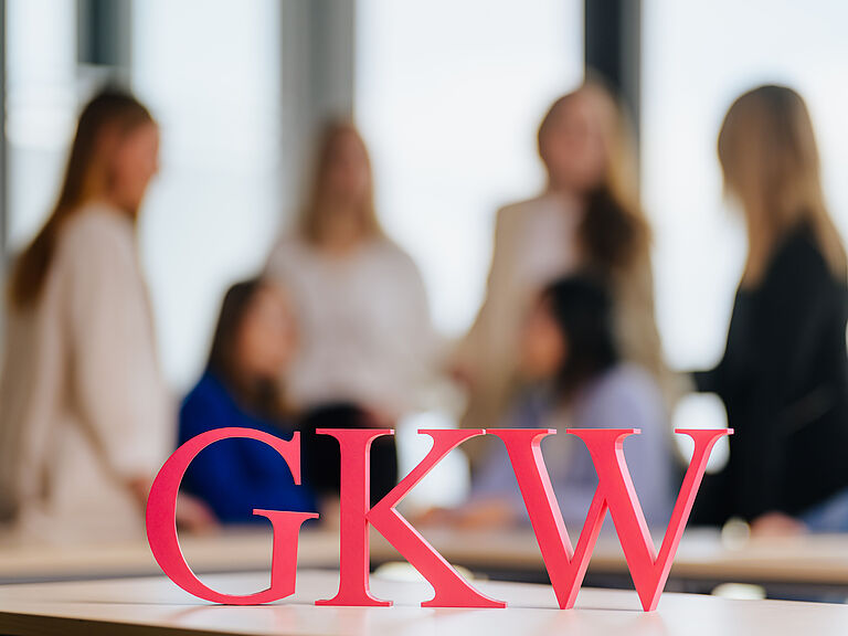 Menschen unscharf im Hintergrund, im Vordergrund die Buchstaben GKW.