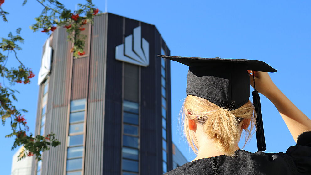 Person mit Talar und Talarhut vor der Universität Paderborn.