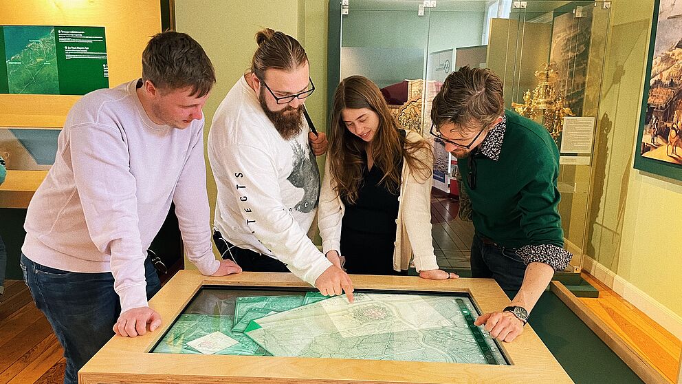 4 Personen stehen um eine digitalen Karte Flanderns herum, studieren, forschen und diskutieren