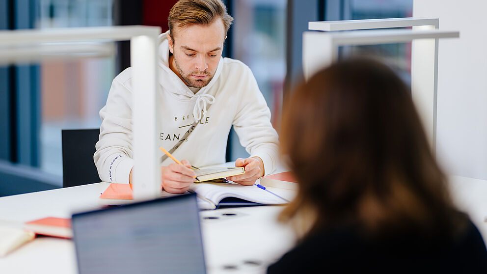 Zwei Personen arbeiten in einem Gruppenraum am Laptop.