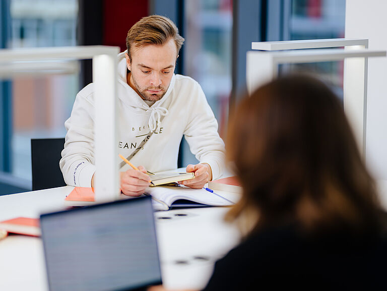 Zwei Personen arbeiten in einem Gruppenraum am Laptop.