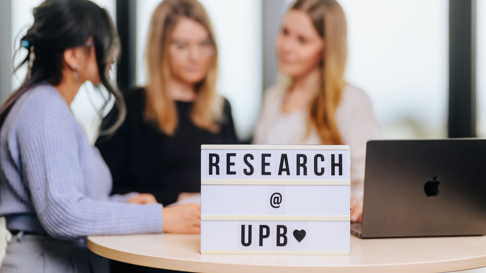 Drei Personen, im Vordergrund ein Leuchtkasten mit dem Text "Research UPB".