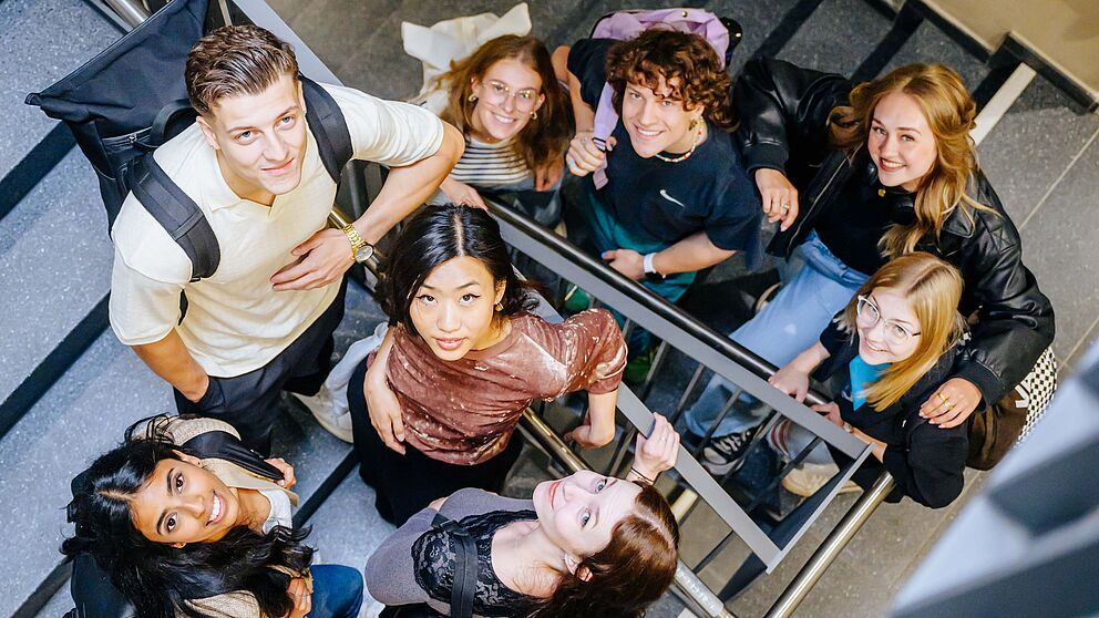 Junge Menschen stehen zusammen im Treppenhaus und schauen nach oben in die Kamera