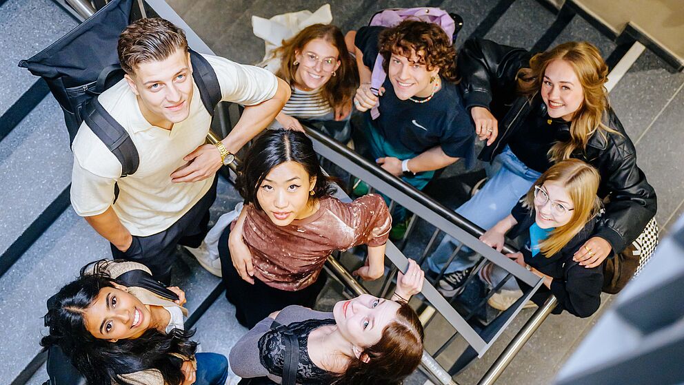 Junge Menschen stehen zusammen im Treppenhaus und schauen nach oben in die Kamera