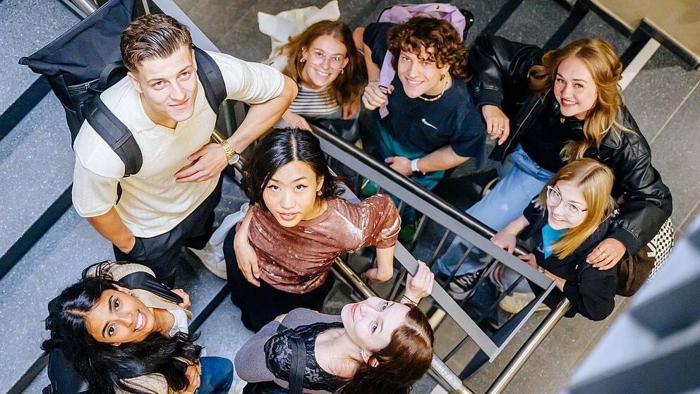 Junge Menschen stehen zusammen im Treppenhaus und schauen nach oben in die Kamera