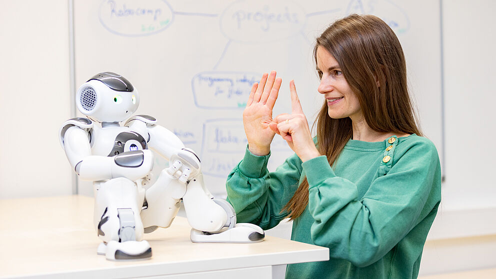 Eine Frau kommuniziert mit den Händen mit einem kleinen Roboter.