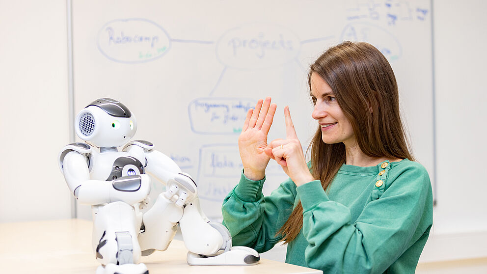 Eine Frau kommuniziert mit den Händen mit einem kleinen Roboter.