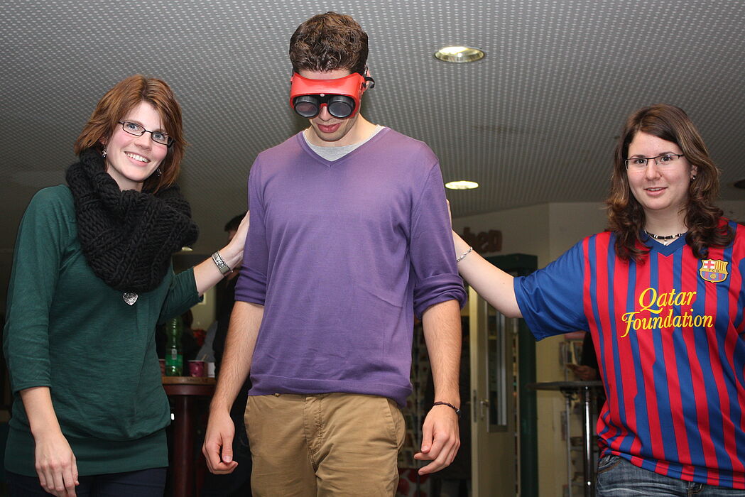 Foto (Universität Paderborn, Patrick Kleibold): Mit den Augen eines Angetrunkenen: Henrik Jahns versuchte mit der Suchtbrille einer Linie zu folgen. Nele Tiedemann (links) und Isabell Schwartz mussten ihm dabei behilflich sein.