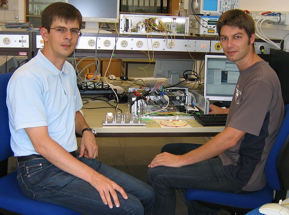 Foto (Universität Paderborn): V. li.: Dr.-Ing. Vitali Mirvoda und Dipl.-Ing. Benjamin Koch arbeiten an ihrem Versuchsaufbau zur unterbrechungsfreien Polarisationsregelung.