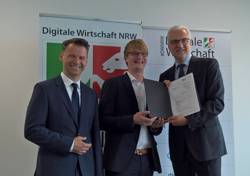 Foto (Universität Paderborn, TecUP): Prof. Dr. Tobias Kollmann (l.) und NRW-Wirtschaftsminister Garrelt Duin (r.) überreichen Dr. Sebastian Vogt (m.), Geschäftsführer von TecUP, den offiziellen Förderbescheid.