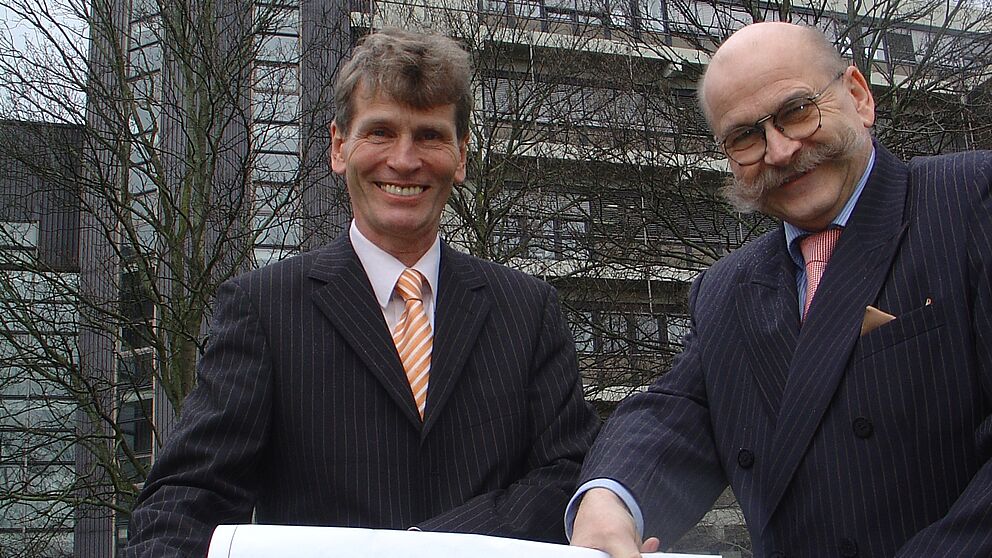Foto (Tibor Werner Szolnoki, Universität Paderborn): Präsident Prof. Dr. Nikolaus Risch (li.) und Kanzler Jürgen Plato bei der künftigen Baustelle mit der Ansicht des geplanten Laborgebäudes auf dem Uni-Campus.