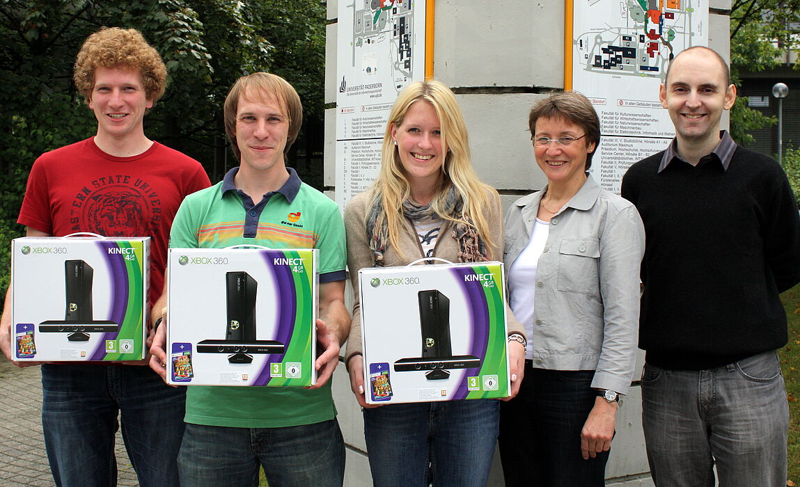 Foto (Uni Paderborn, Patrick Kleibold): (v. r.) Tobias Oetterer und Dr. Gudrun Oevel (beide vom IMT) überreichten den Studierenden Carina Doettger, Tim Gemmeke und Timo Schlüßler die XBoxen.