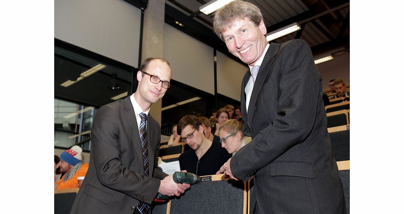 Foto (Universität Paderborn, Vanessa Dreibrodt): Dr. Oliver Middendorf, HLB Stückmann, (li.) bringt im Hörsaal die Plakette am „Leerstuhl“ an. Darüber freut sich Prof. Dr. Nikolaus Risch.