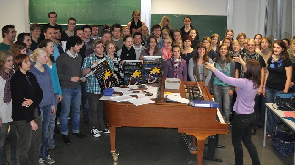 Foto (Universität Paderborn, Mark Heinemann): Es wird fleißig geübt: Die Sängerinnen und Sänger von UniSono proben unter der Leitung von Gundula Hense (am Klavier) bereits seit April für das Adventskonzert.