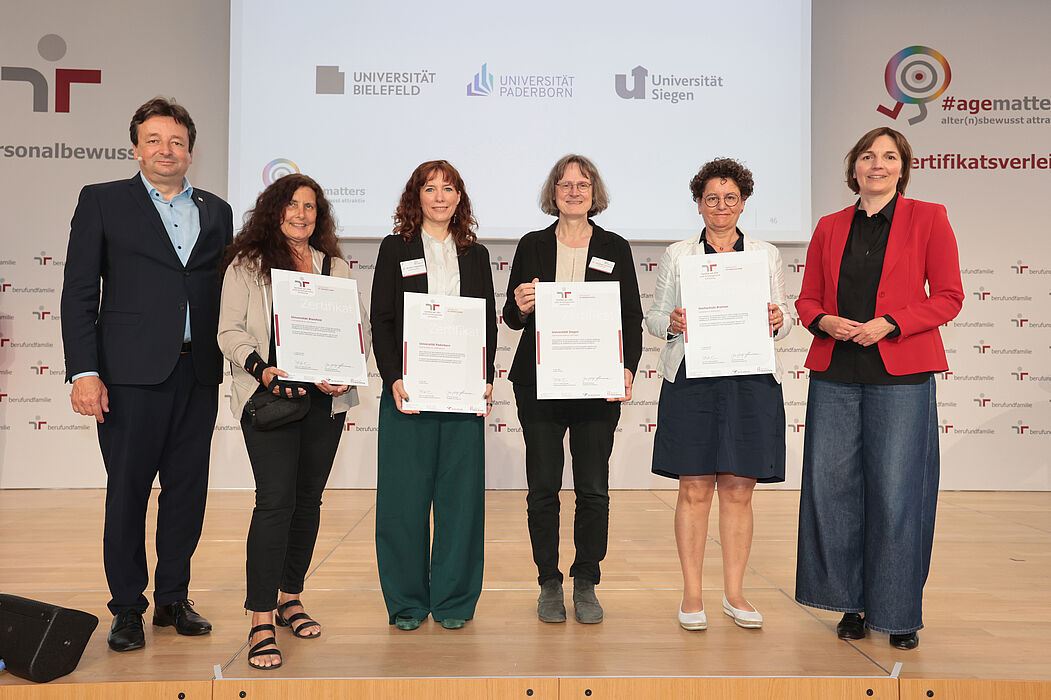Ein Mann links und daneben fünf Frauen stehen in einer Reihe. Die vier Frauen in der Mitte halten Zertifikate in der Hand und halten diese in die Kamera.
