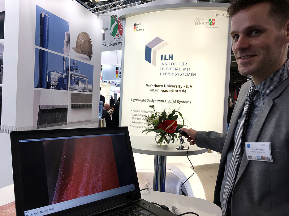 Foto (ILH): Am ILH Messestand können Besucher Proben mithilfe eines USB Minimikroskops betrachten. Hier demonstriert der Kollegiat Jörn Achtelik, Mitarbeiter des Lehrstuhls für Nanostrukturierung, Nanoanalytik und Photonische Materialien von Prof. Lind