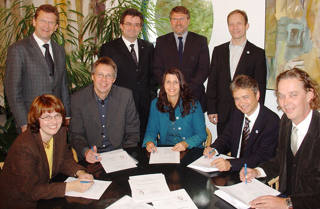 Foto (Mark Heinemann): (v.li.) Prof. Dr. Norbert Olivier, Martin Hornberger, Ulrich Kramer, Raphael Lorenz und am Tisch sitzend Dr. Katja Ullrich, Christoph Schlösser, Claudia Reichold, Prof. Dr. Bernd Frick sowie Uwe Diedam während der Unterzeichnung d