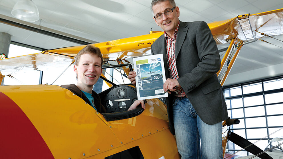 Bild: Jonas Homburg nimmt seinen Preis vom Chef des Flughafens Paderborn-Lippstadt Elmar Kleinert in einer Boeing Stearman PT-17 aus dem Jahr 1941 entgegen.