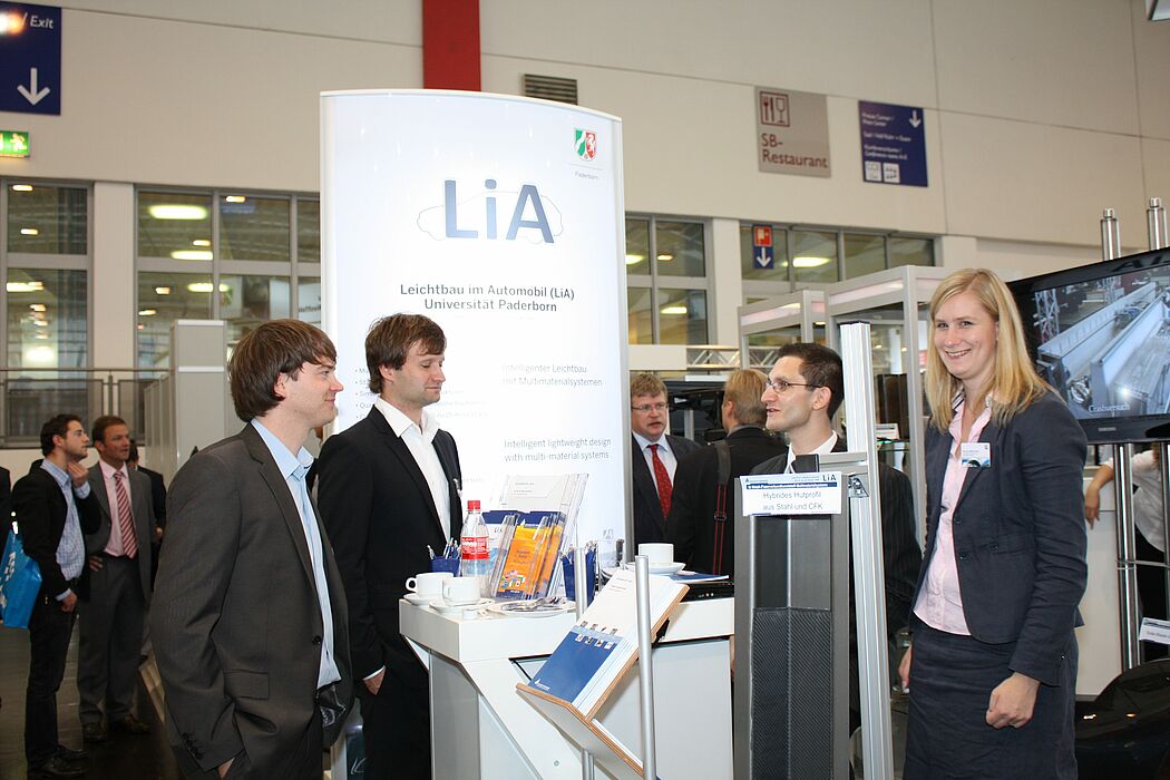 (Universität Paderborn, Fakultät für Maschinenbau): (v.l.n.r.) Zwei Fachbesucher der Messe im Gespräch mit Dipl.-Ing. Dipl.-Wirt.-Ing. Christian Lauter und Dipl.-Ing. Meike Frantz vom Lehrstuhl „Leichtbau im Automobil“.