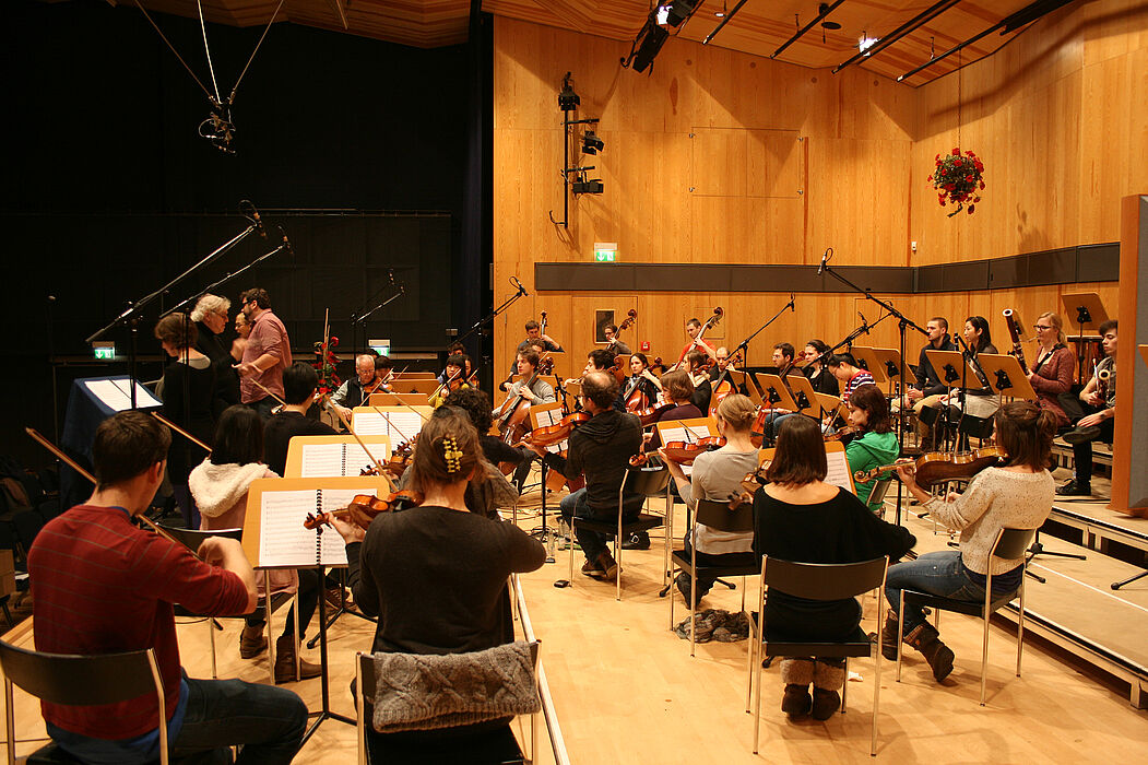 Abbildung: Tonaufnahmen in der Aula der Hochschule für Musik Detmold: Noch liegen gedruckte Noten auf den Pulten der Musiker. Bald können Dirigenten ihre Interpretation der Oper am Computer zusammenstellen und an die Notenständer ersetzende Tablets üb