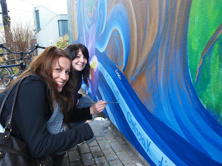 Foto (Universität Paderborn, Martin Decking): Corinna Seifert und Corinna Kunz (v.l.) studieren Kunst sowie Spanisch bzw. Deutsch auf Lehramt im 3. Semester. Hier signieren sie das gemeinsame Kunstwerk.