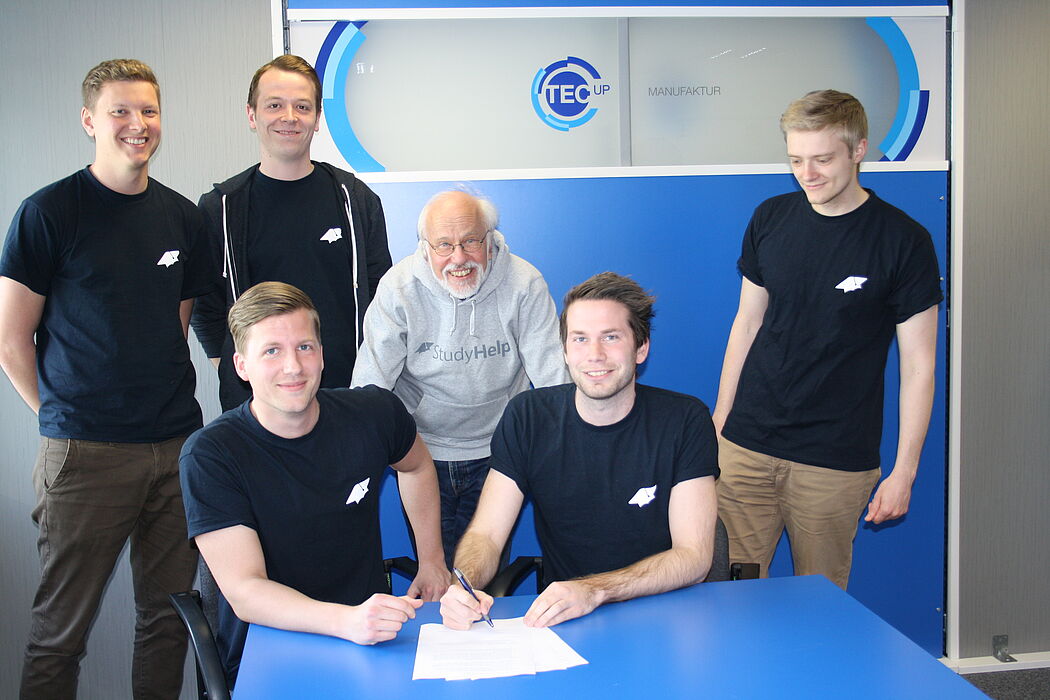 Foto (TecUP, Universität Paderborn): Die beiden Gründer Carlo Oberkönig und Daniel Weiner (vorne, v. l. n. r.) und Dr. Volker Bastert (mittig) unterzeichnen den Gesellschaftsvertrag im Kreise des StudyHelp-Teams um Julian Droste, Maximilian Fleitmann u