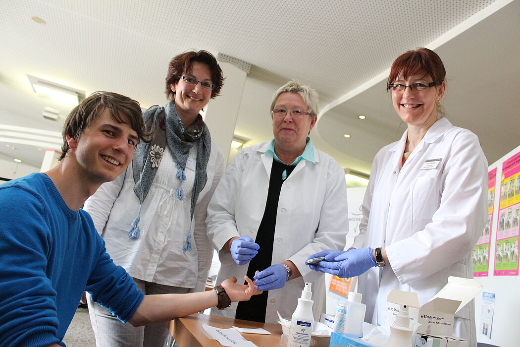 Foto (Universität Paderborn, Heiko Appelbaum): Auch der Student Till Tolckmitt ließ seine Blutzuckerwerte ermitteln. Das Angebot der Arzthelferinnen Elke Pätzold und Christel Lücke (v. r.) vom Betriebsärztlichen Dienst Bethel stieß auf großes Inter