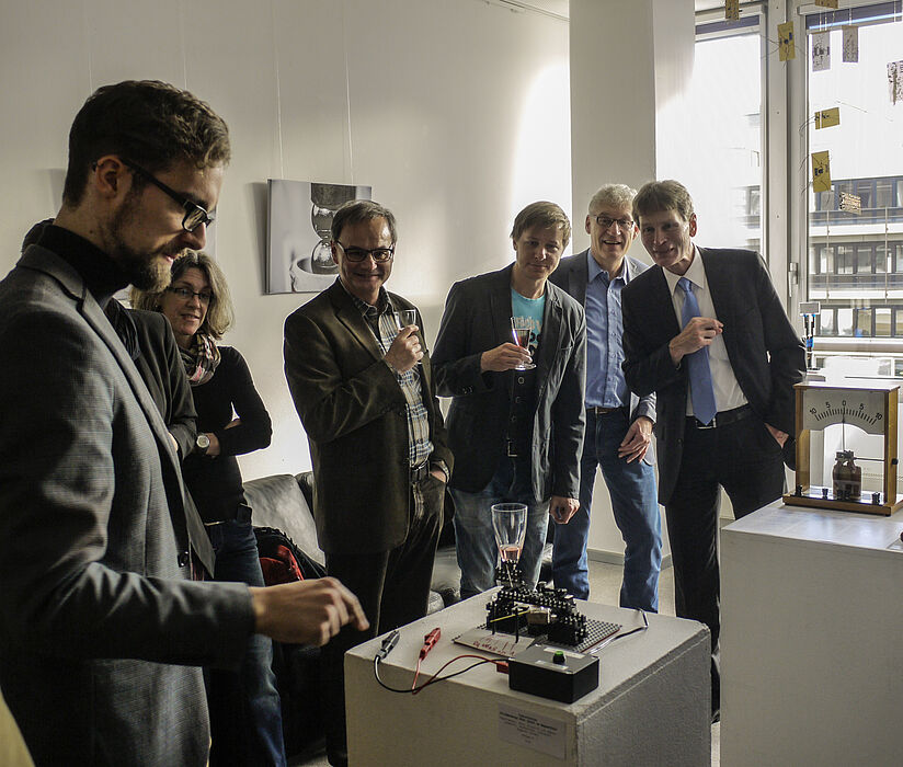 Foto (Heike Probst): Master-Student Johannes Pauly setzt die interaktive Installation unter den neugierigen Blicken von (v. l. n. r.) Prof. Dr. Artur Zrenner, Dr. Marc Sacher, Prof. Dr. Peter Reinhold und Präsident Prof. Dr. Nikolaus Risch in Gang.