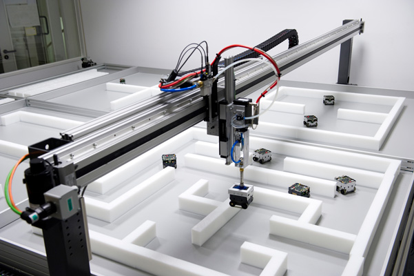 Foto: Der Greifarmroboter der Telewerkbank setzt einen Miniroboter in die Versuchsumgebung für ein Experiment. (© Heinz Nixdorf Institut)