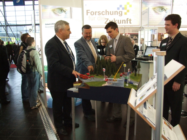 Foto (Lehrstuhl C.I.K): Katastrophenschutz im Miniaturformat: Parl. Staatssekretär Manfred Palmen (Innenministerium NRW) und Staatssekretär Karl Peter Brendel (Innenministerium NRW) mit Dipl.-Ing. Jens Pottebaum und Dipl.-Wirt.-Inf. Benedikt Birkhäuser