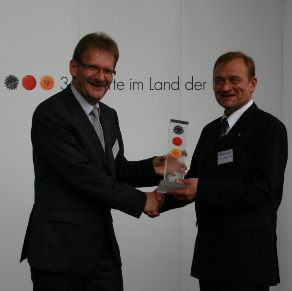 Foto (C.I.K.): Thomas Liedmeyer (r.) übergibt Prof. Dr.-Ing. Rainer Koch die Auszeichnung als „Ausgewählter Ort im Land der Ideen“.